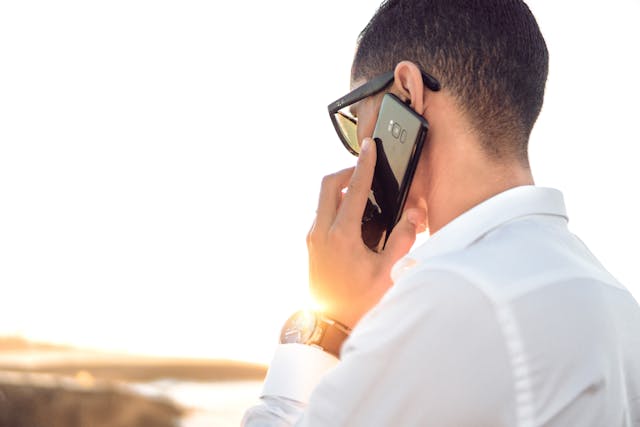 Person wearing sunglasses while holding a cellphone to their ear